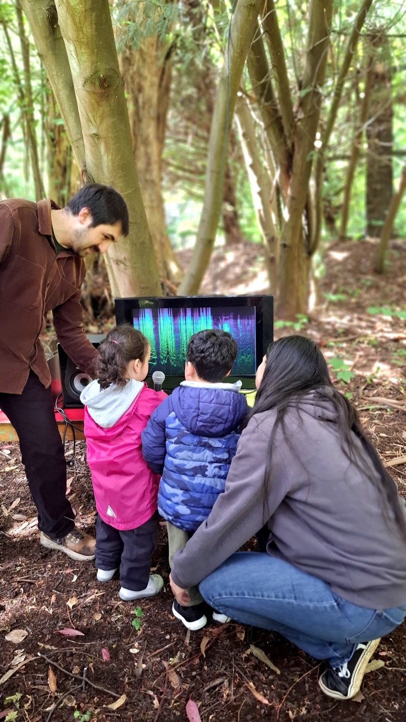 Niños y niñas explorando espectrogramas de sonido en el bosque